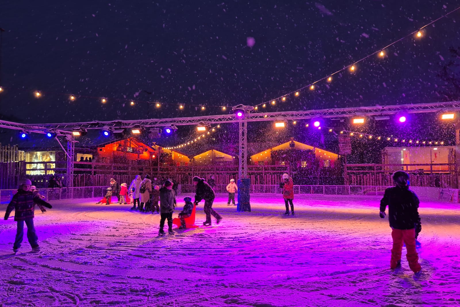Eisfeld bei Nacht unter violetten Scheinwerfern, Lichterketten und Schneefall